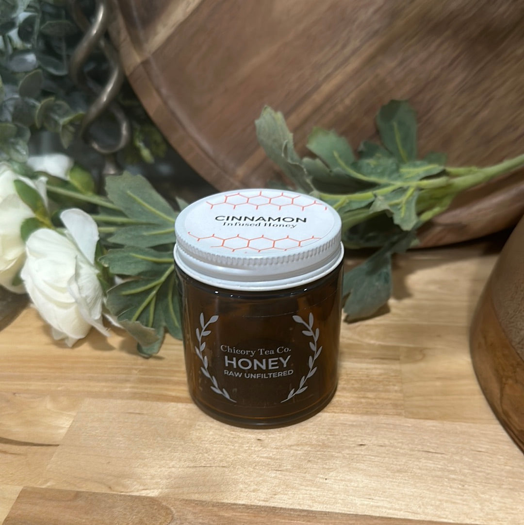 An artistic product photo of Chicory Tea Co.'s Cinnamon Honey in the jar, view from the front with flowers and barrel in the background