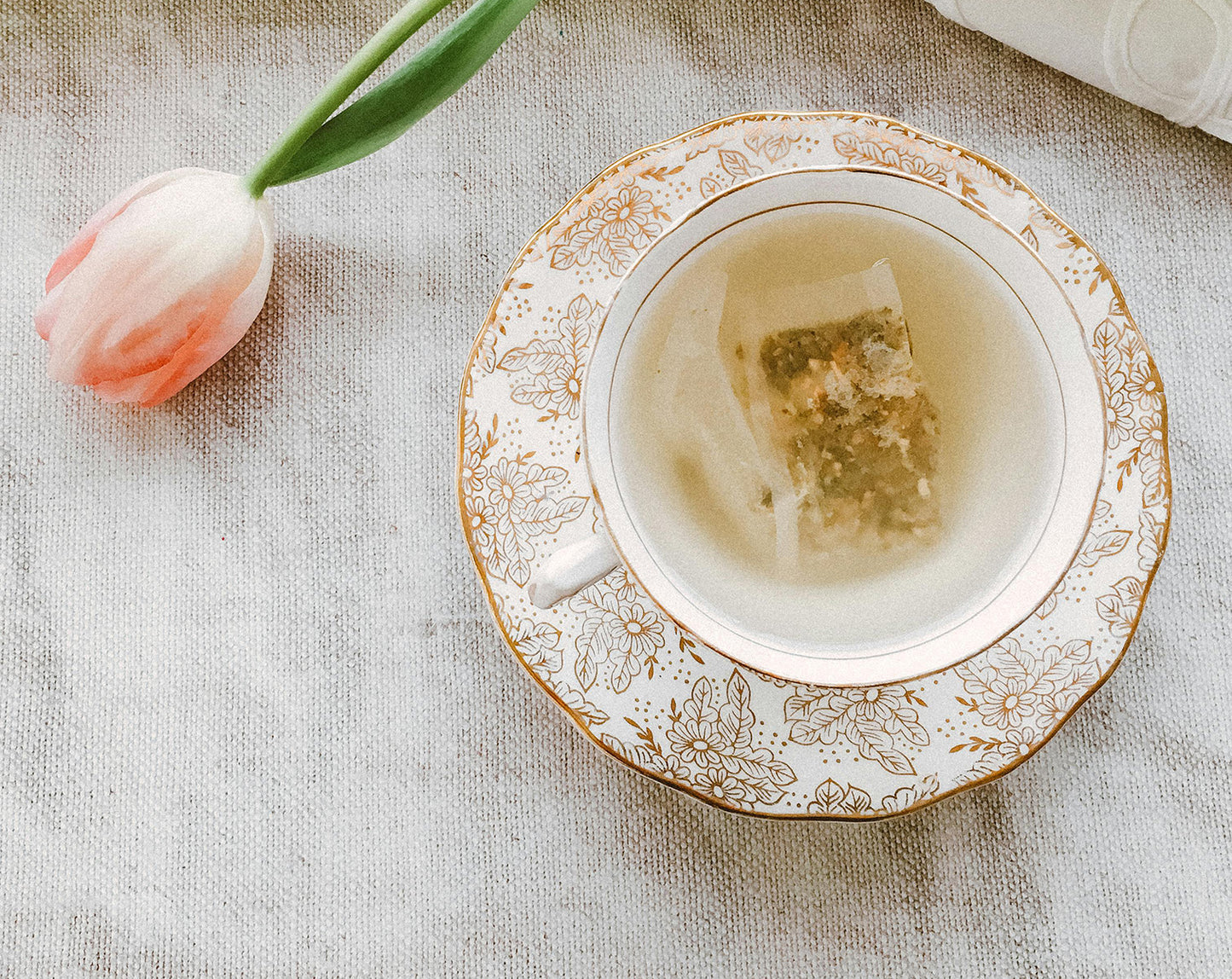 An artisitic photo of a tea bag being steeped in a cup with the flower being laid off to the side