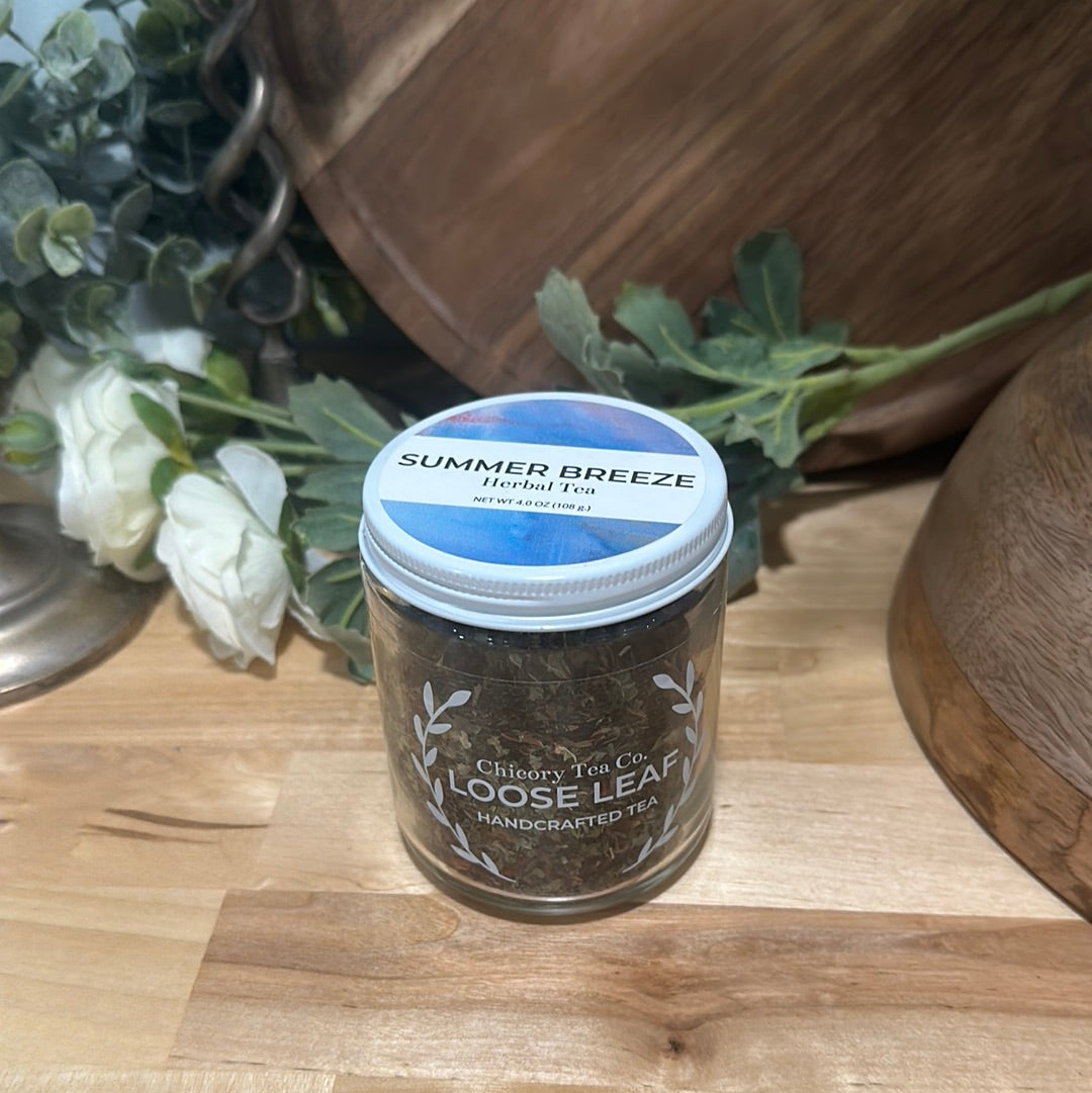 Chicory Tea Co.'s Summer Breeze in the jar, view from front on a wood floor with flowers and barrel in the background