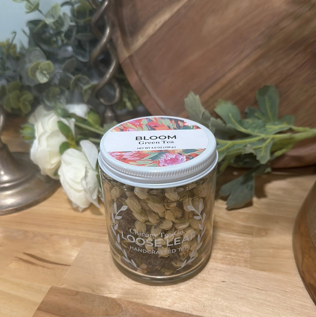 An artistic product photo of Chicory Tea Co.'s Bloom Green Tea in the jar, view from front with flowers and barrel in the background