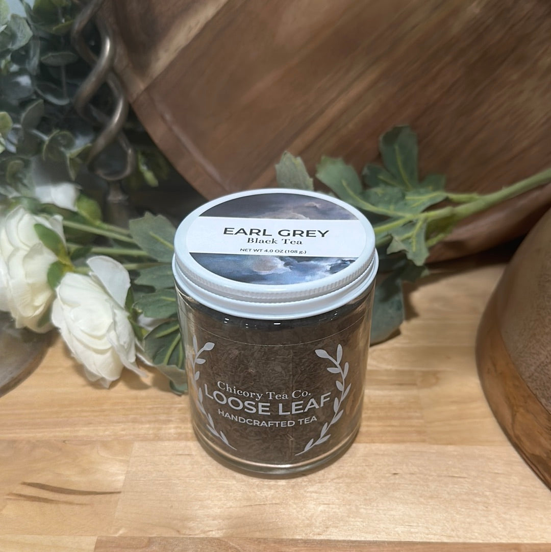 An artistic product photo of Chicory Tea Co.'s Earl Grey Black Tea in the jar, view from front with flowers and a barrel in the background