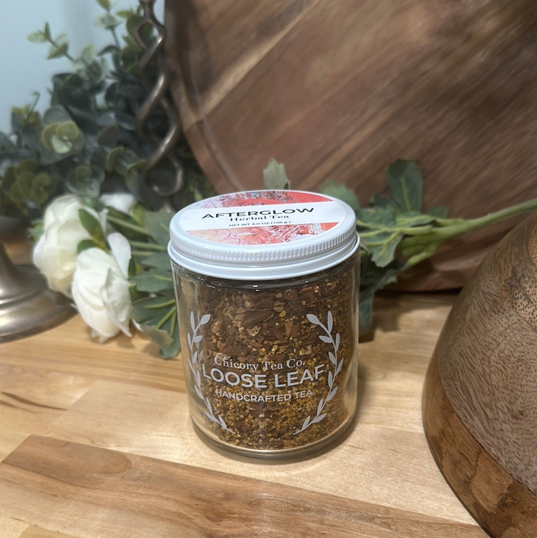 An artistic product photo of Chicory Tea Co.'s Afterglow Herbal Tea in jar, view from front with flowers and barrel in the background