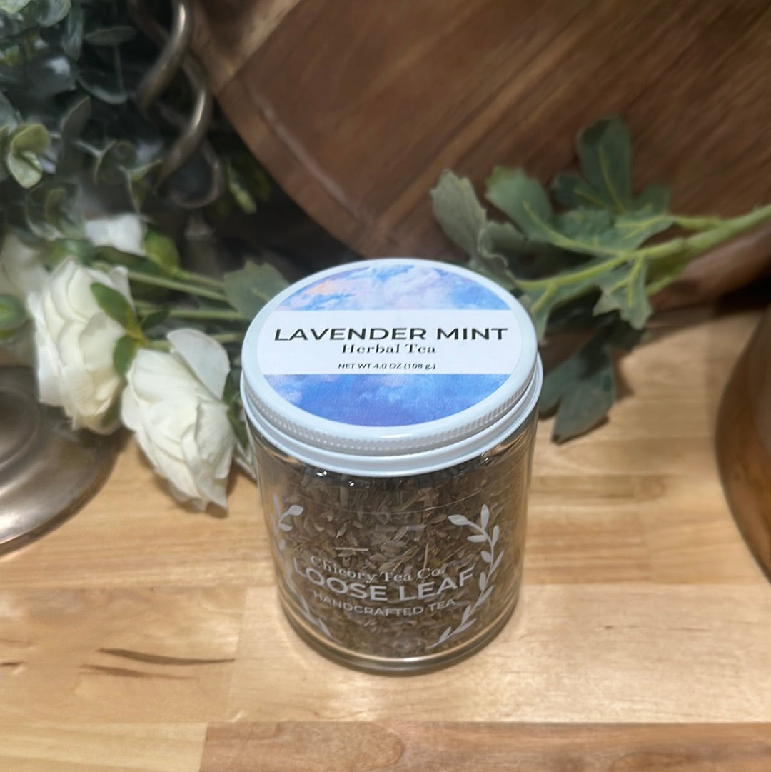 An artistic product photo of Chicory Tea Co.'s Lavender Mint in the jar, view from front on a wood floor with flowers and a barrel in the background