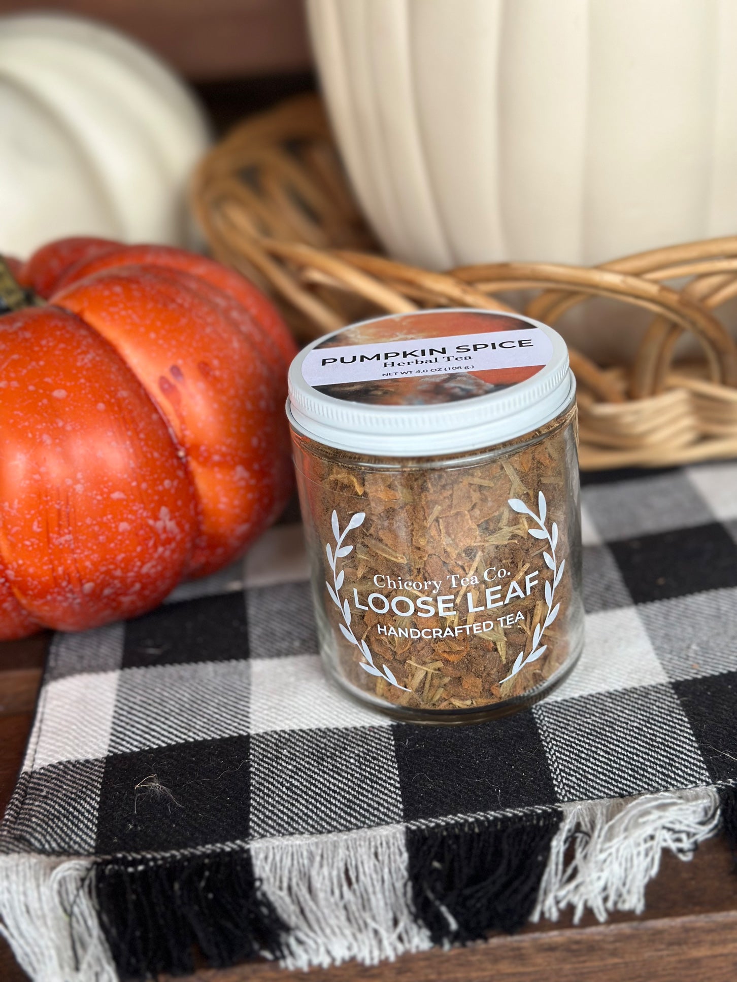 An artistic version of Chicory Tea Co.'s Pumpkin Spice Herbal Tea with pumpkins on the background, sitting on a checkered blanket